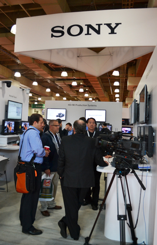 People standing near video cameras and monitors at a Sony production systems display.