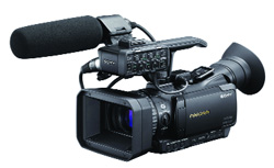 A black professional Sony video camera equipped with a large shotgun microphone and a lens hood.