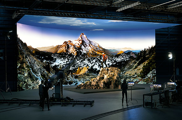 A film studio with a giant curved LED screen showing a snowy mountain range behind a rocky set piece.