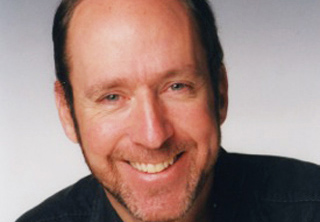 A smiling man with light skin, short brown hair, and a beard looking toward the camera.