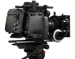 A professional black cinema camera equipped with a large lens and accessories mounted on a tripod.