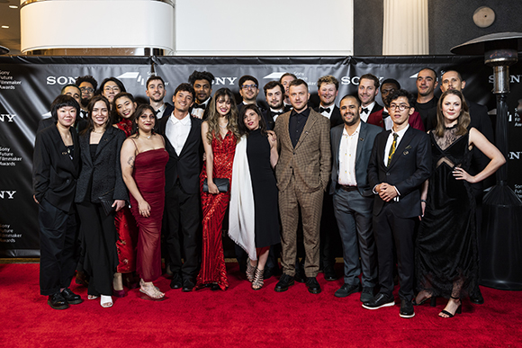 A diverse group of people in formal attire posing on a red carpet in front of a Sony backdrop.