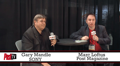 Gary Mandle and Marc Loftus sit at a small table holding microphones against a black backdrop.