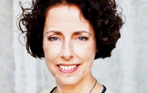 A close-up portrait of a woman with dark curly hair smiling at the camera.