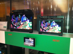 Two professional monitors, one larger than the other, display colorful abstract graphics. Both monitors have rack-mounted equ