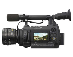 A professional black digital video camera with a large lens, microphone, and LCD screen.