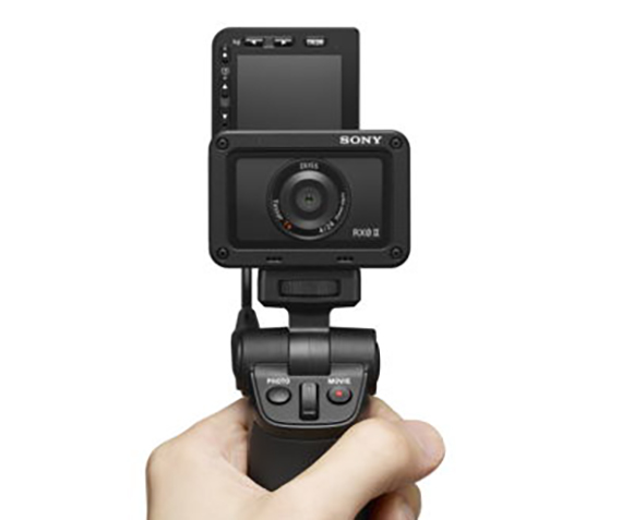 A hand holds a black Sony RX0 II camera mounted on a small handheld gimbal stabilizer.