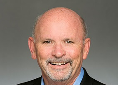 A smiling man with a bald head and a graying goatee against a gray background.