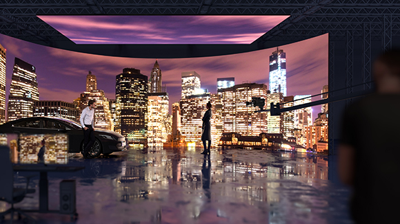 A film crew works in a studio with a massive curved LED screen showing a glowing city skyline at night.