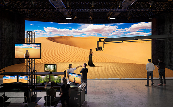 Film crew in a studio using a large curved LED screen displaying a desert landscape for virtual production.