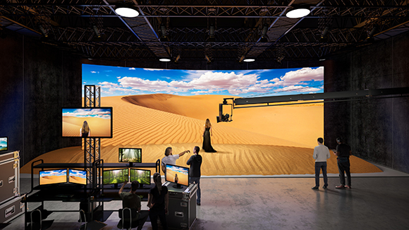 Film crew in a studio using a large curved LED screen displaying a desert landscape.