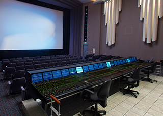 A long, professional audio mixing console with numerous sliders and buttons in a darkened theater.