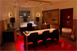 A music recording studio control room with mixing desks, monitors, and several black office chairs.