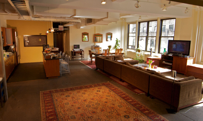 A spacious open-concept room featuring a kitchen, a long dining table, and a large brown sectional sofa.