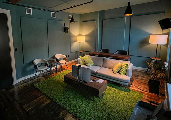 A modern living room with a green rug, a grey sofa, a wooden coffee table, and two warm lamps.