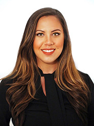 A smiling woman with long, wavy brown hair wearing a black top against a white background.