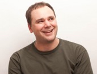 A man with short brown hair smiling and looking up and to the side against a white background.