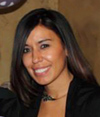 A smiling woman with long dark hair wearing a black top and a necklace.