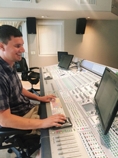 A man smiling while operating a large professional audio mixing console in a studio.