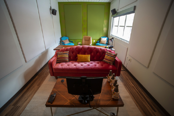 A red tufted sofa sits in a small room with green walls, two blue chairs, and a wooden coffee table.