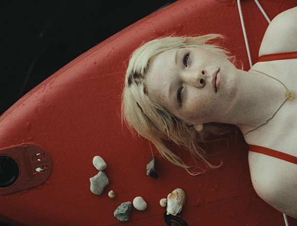 A person with blonde hair lies on a red textured surface next to several small stones.