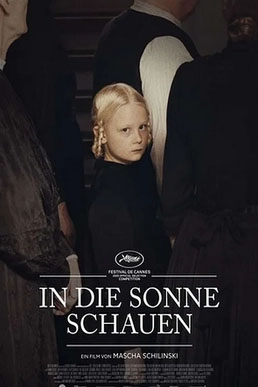 A young blonde girl in dark clothing looks forward, surrounded by the backs of several adults in dark attire.