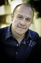 A man with short dark hair and a dark blue button-down shirt looking toward the camera.