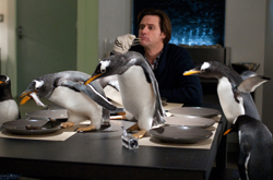 A man sits at a dining table surrounded by several penguins standing on the table.