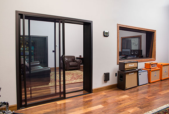 Sliding glass doors lead into a lounge area next to a studio window and guitar amplifiers.