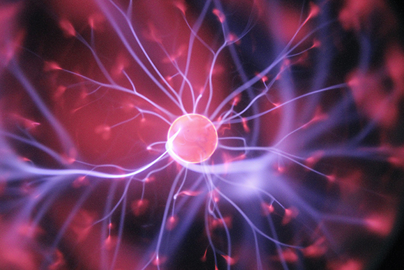 Purple and red electrical filaments radiating from a central glowing sphere in a plasma globe.