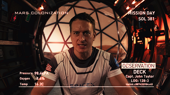 A man in a white SpaceX shirt looks at the camera inside a spacecraft with a large circular window behind him.