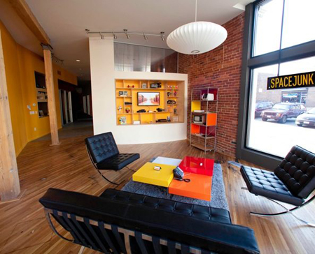 A modern living room with black leather chairs, a colorful coffee table, and a large window.