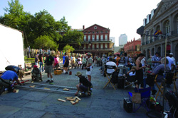 People sitting and standing in a paved plaza surrounded by multi-story brick buildings.