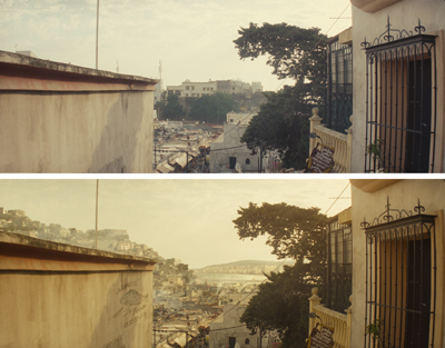 A view from a balcony overlooking a hillside town with dense buildings and trees under a hazy sky.