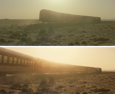 A long passenger train moves through a vast, scrubby desert under a bright, hazy sunset.