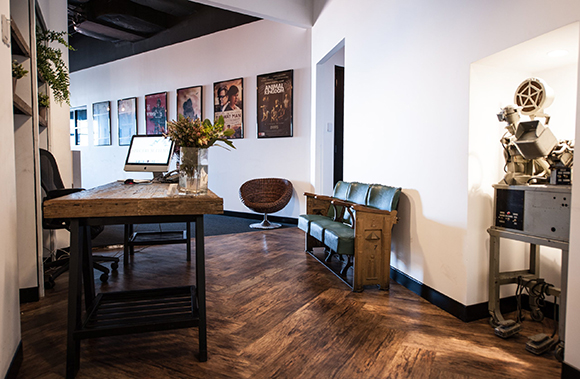 Office interior with a wooden desk, computer, movie posters, and a vintage-style green bench.