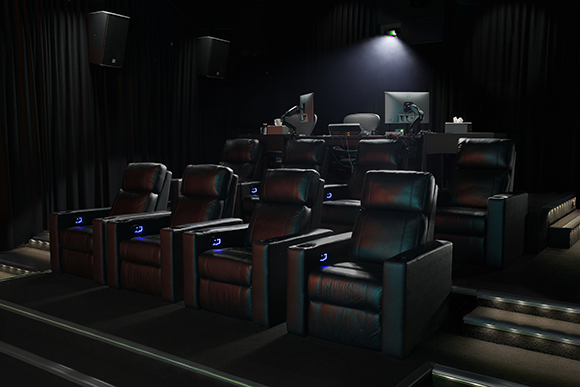 Rows of black leather reclining theater seats in a dark room with a projection booth in the background.