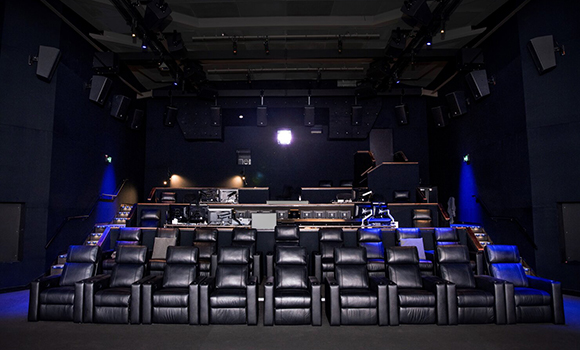 Rows of black leather reclining seats facing a projection screen in a dark cinema theater.