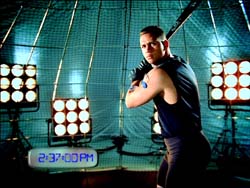 A man in a black tank top poses in front of studio lights and a large net background.