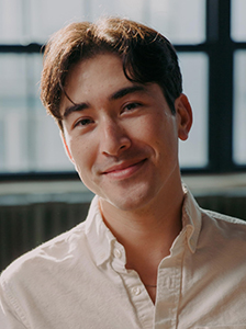 A smiling young man with dark wavy hair wearing a white button-down shirt.