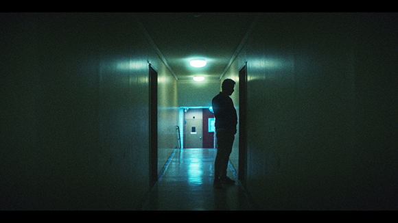 Silhouette of a person standing in a dark, narrow hallway illuminated by overhead lights.