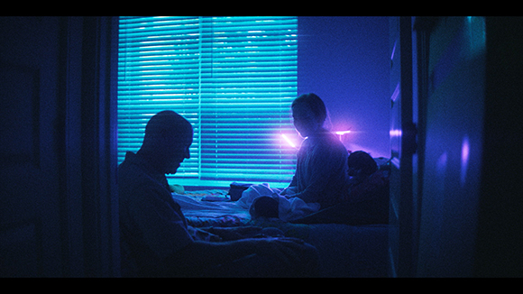 Silhouettes of people in a dark room illuminated by blue light through blinds and a purple glow.