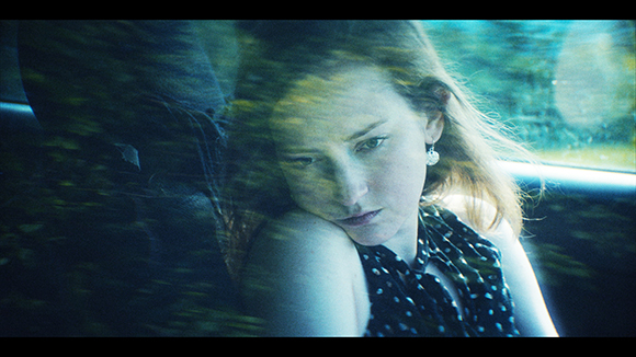 A young woman with long hair looks pensively out of a car window during a ride.