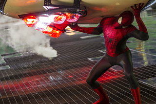 A person in a red and black Spider-Man suit holds up a large, glowing mechanical device emitting red light and smoke.
