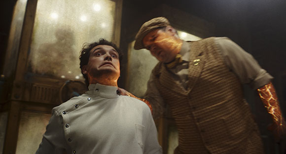 A man in a white coat looks up in fear as another man with glowing orange veins on his arm places a hand on his shoulder.