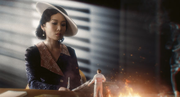 A woman in a wide-brimmed hat and vintage clothing looks down at a tiny figure in a white suit standing near a large fire.