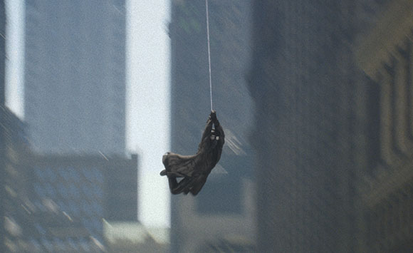 A dark silhouette of a person swinging on a thin line between tall city buildings.