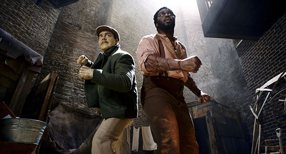 Two men in a narrow alleyway, one wearing a cap and green jacket, the other in suspenders and a light shirt, both looking up