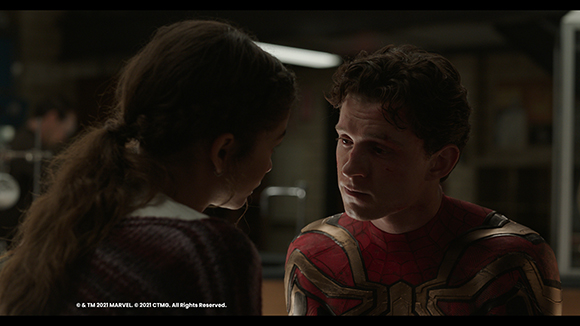 A man in a red and gold suit looks intensely at a woman with long brown hair in a dark setting.