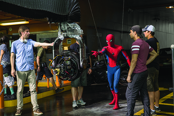 A film crew works around an actor in a Spider-Man suit and a large camera rig on a movie set.